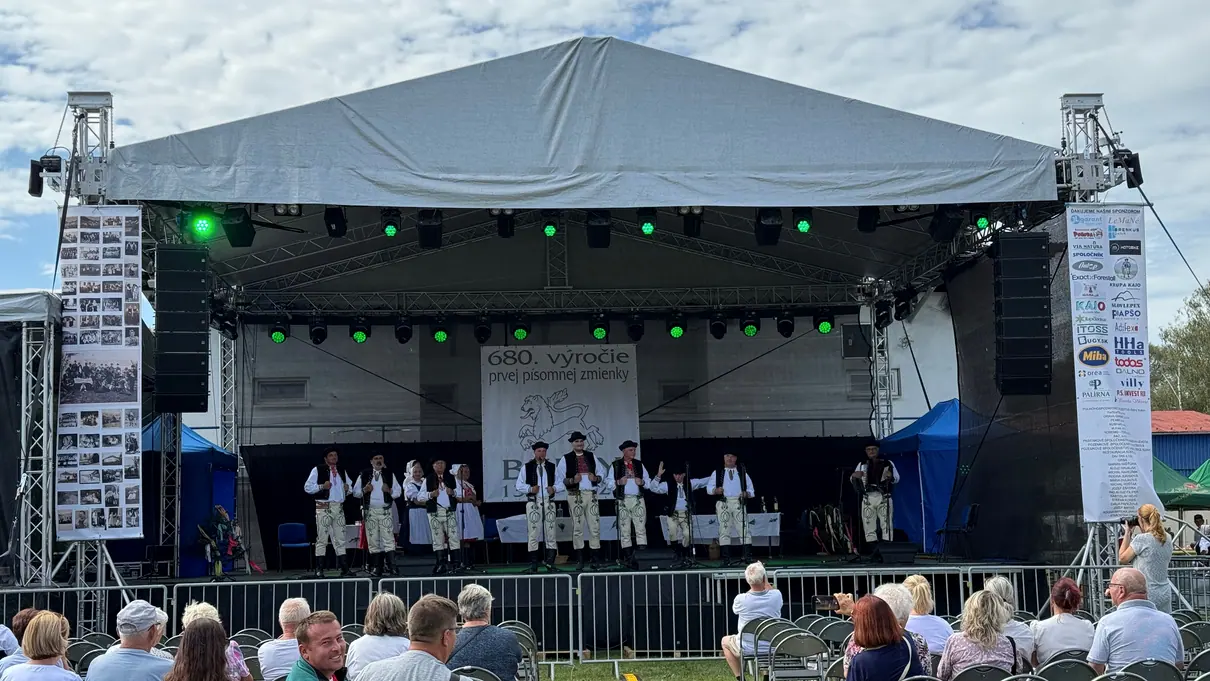 Folklórny súbor na pódiu s transparentom 680. výročia obce Bziny