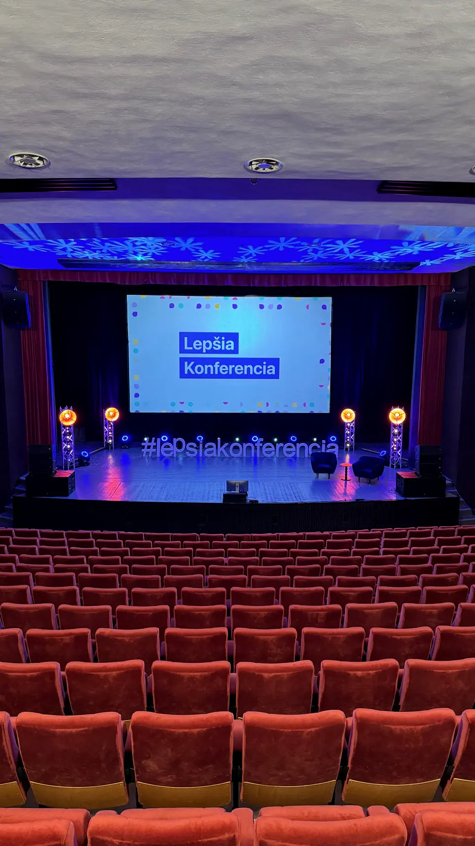 Divadelná sála s pódiom a nápisom Lepšia Konferencia na plátne