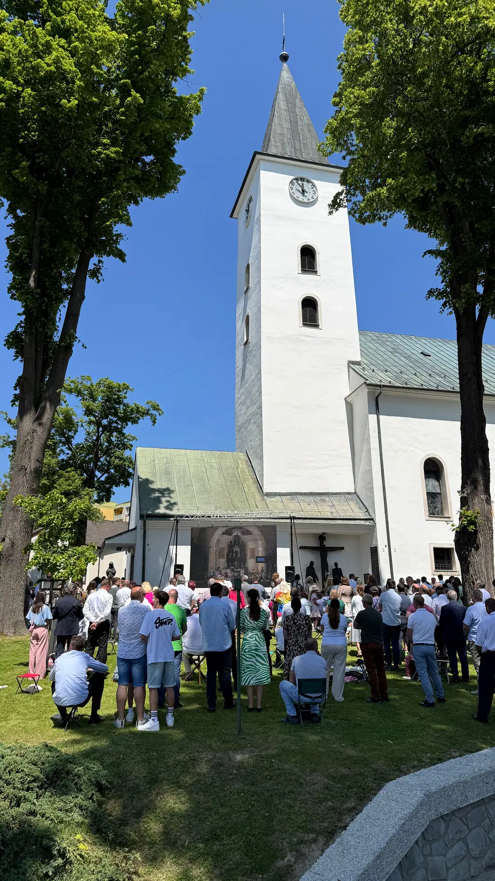 Veriaci zhromaždení pred kostolom s obrazovkou pre prenos slávnostnej svätej omše
