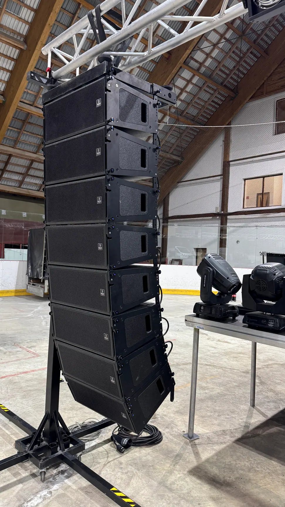 Line array zavesený na truss konštrukcii v hale, vedľa pohyblivé svetlá